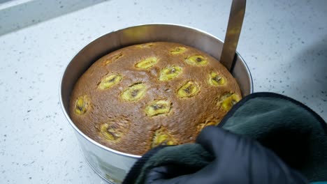 the process of removing the banana cake from a baking tray. the cake surface is carefully separated from the baking tray using a long spatula. the cake will be transferred to the cake board.