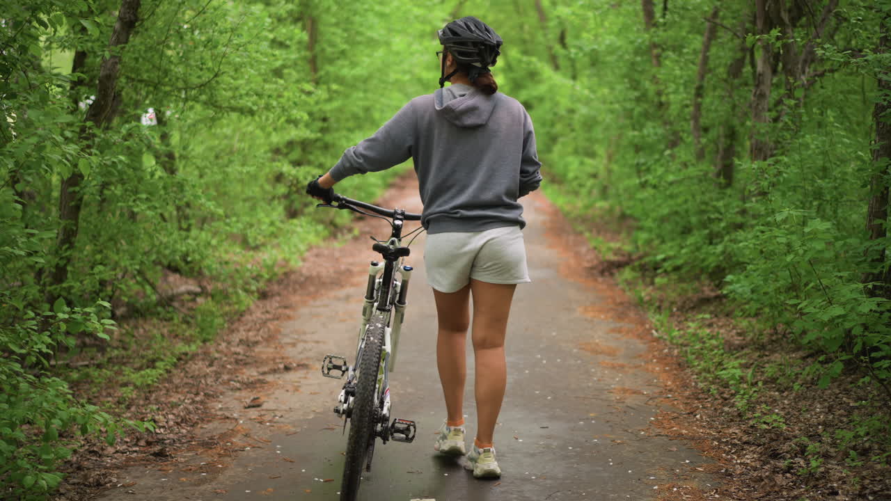 Woman Walking Bike Through Foliage, Female Rider Moving Through Leafy Pathway Confidently, Back Perspective Of Woman Walking Her Bicycle Through Dense Leafy Tunnel With Purposeful Stride