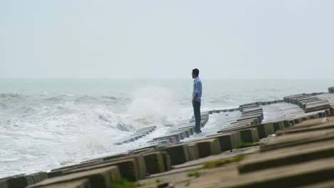 Un-Hombre-Solitario-Parado-Junto-Al-Mar-Con-Muros-De-Piedras-Y-Olas-Rompientes