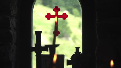 view from inside out through the window of a bulgarian orthodox chapel. burning candles against a background of a red cross painted on glass. racking focus. silhouette. eastern orthodox church.