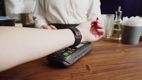 paying with smartwatch in cafe. contactless, touch-free shopping in pubs. nfc technology concept, using fitness bracelet payment via terminal close-up.