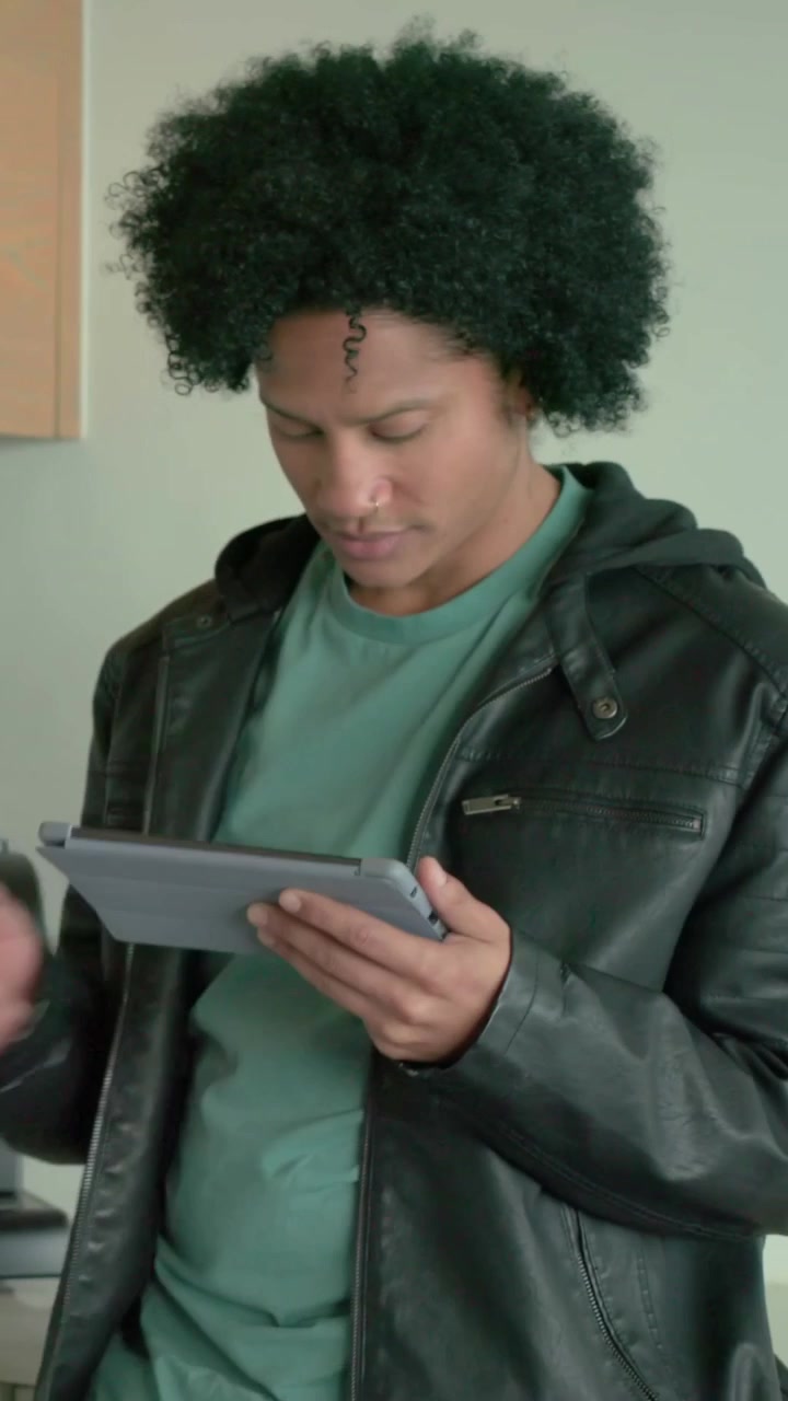 Video verticale: Uomo in giacca che legge un tablet, tocca lo schermo in cucina, controlla un elettrodomestico, alzando lo sguardo