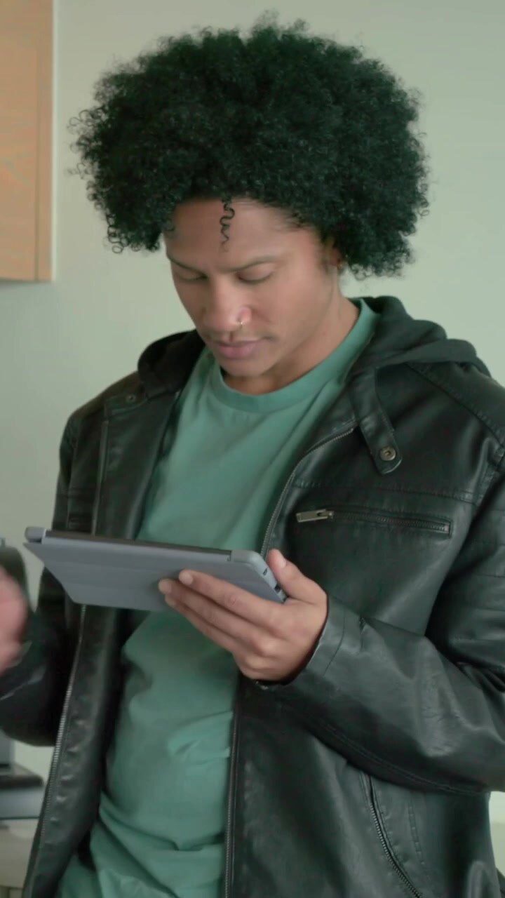 Vertical video: Reading tablet, man in jacket tapping in kitchen, checking appliance, glancing up