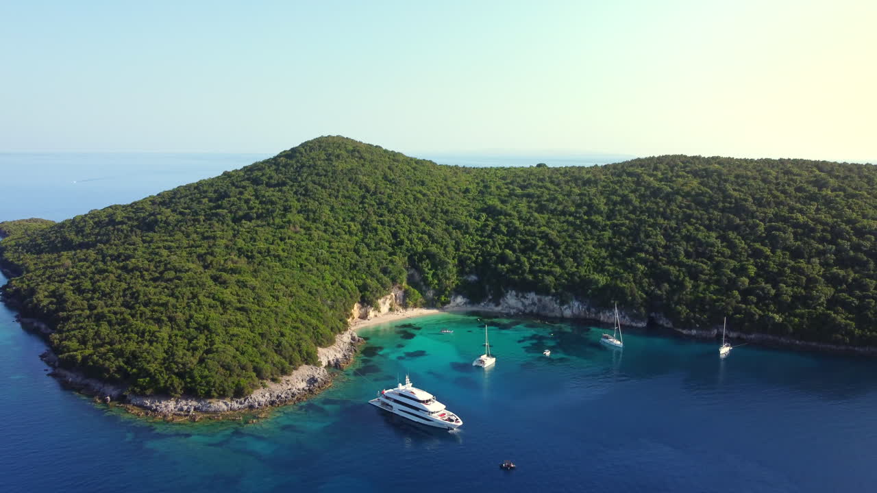 Ampio sorvolo aereo laterale dell'iconica spiaggia Blue Lagoon, Sivota, Grecia, con yacht di lusso nel Mar Ionio cristallino e turchese.