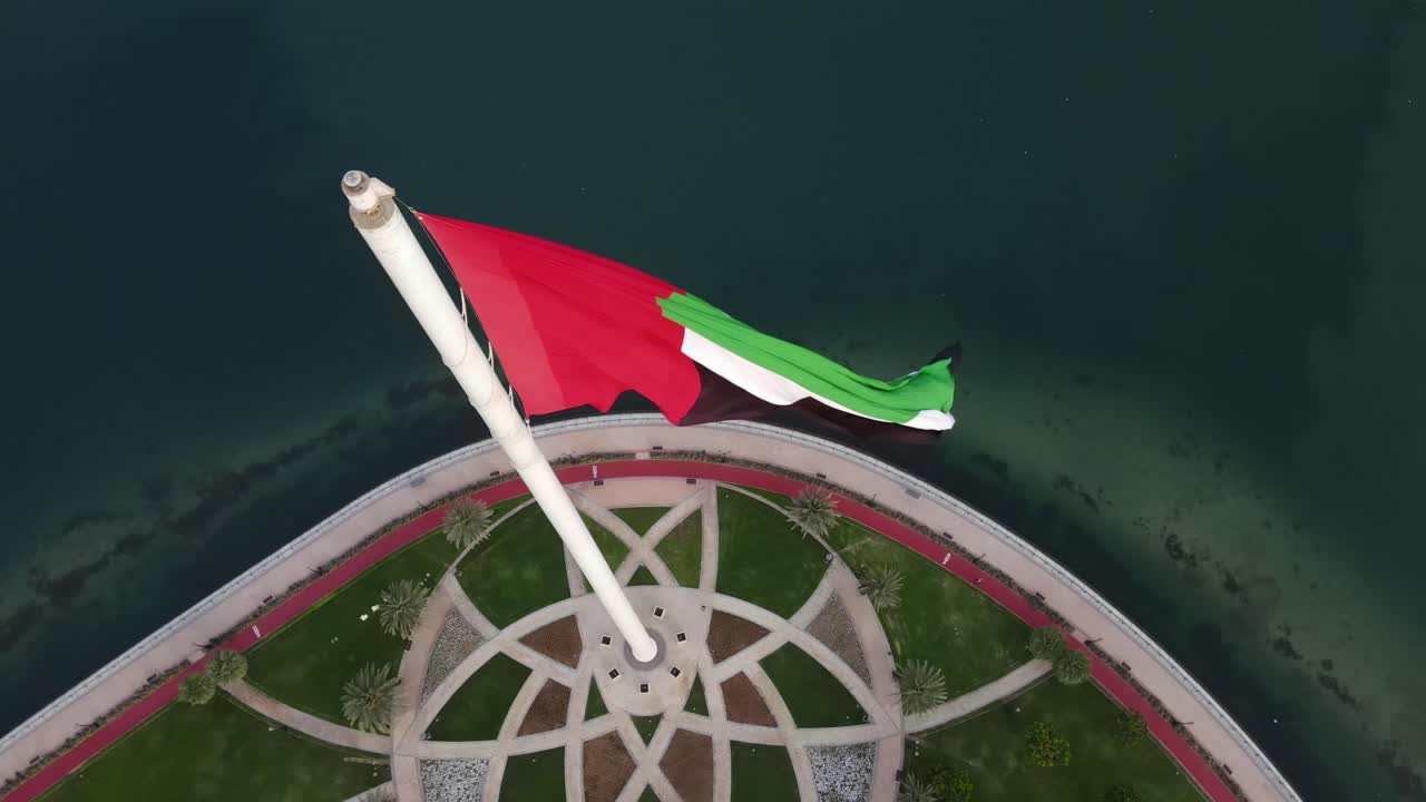 4k: impresionante dron de cerca, bandera de los emiratos árabes unidos ondeando en el viento sobre la isla de la bandera de sharjah, emiratos árabes unidos, video 4k