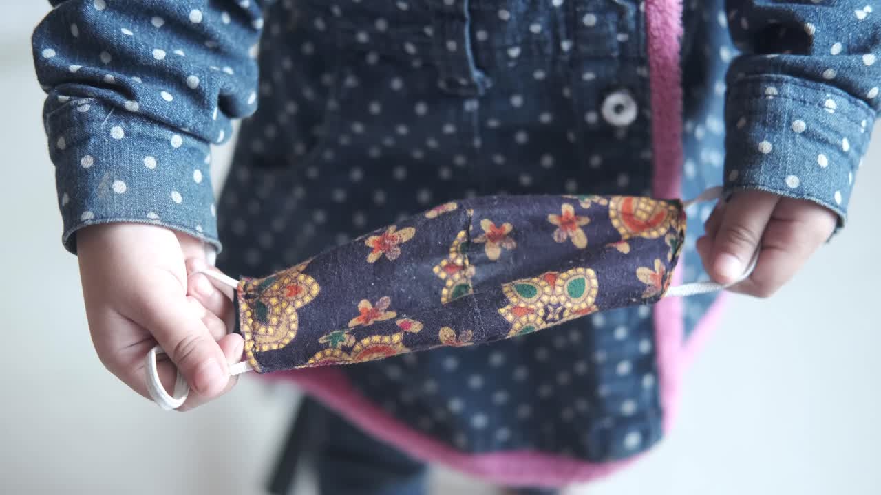 패턴 된 천 얼굴 마스크 를 들고 있는 아이