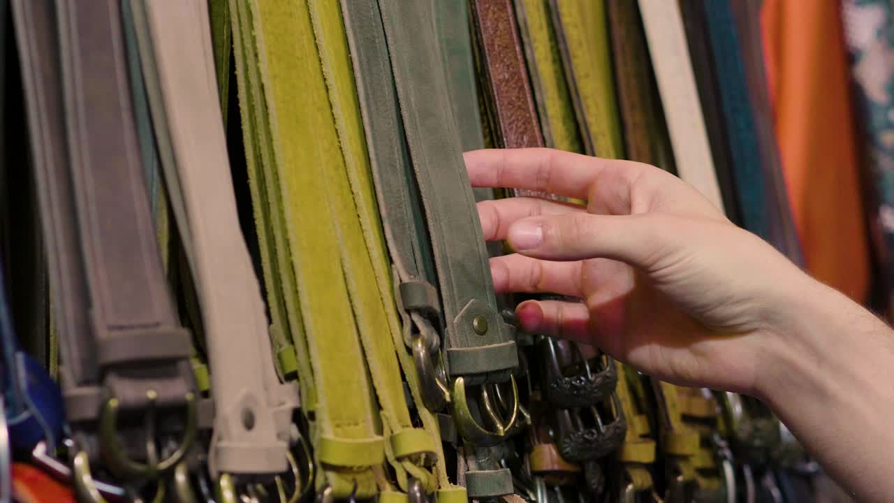 가죽의 혼합물과 다른 색상의 가죽 벨트, 그리고 재료의 품질을 테스트하기 위해 만지는 손.