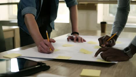 Two-Businessmen-Is-Pointing-At-The-Table-With-Yellow-Papers-On-It-With-The-Pencils-In-Business-Meeting