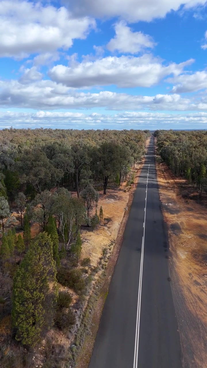 Ripresa aerea con drone di una lunga strada asfaltata attraverso la boscaglia australiana sotto un cielo nuvoloso
