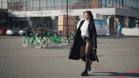 confident lady walking to a business meeting, dressed in a stylish black coat and boots, with someone walking behind her on a busy urban street with parked bicycle