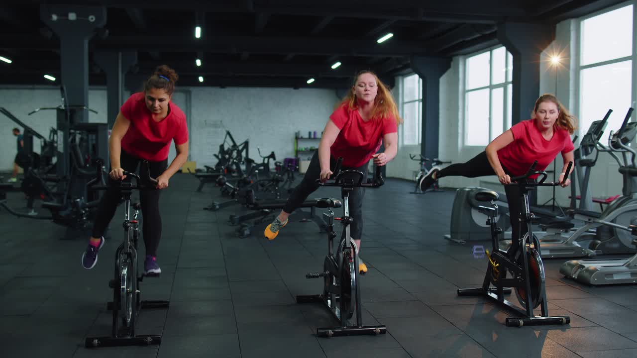 Group of smiling friends women class exercising training spinning on stationary bike at modern gym