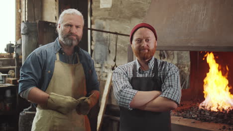 portrait of two blacksmiths by forge in smithy