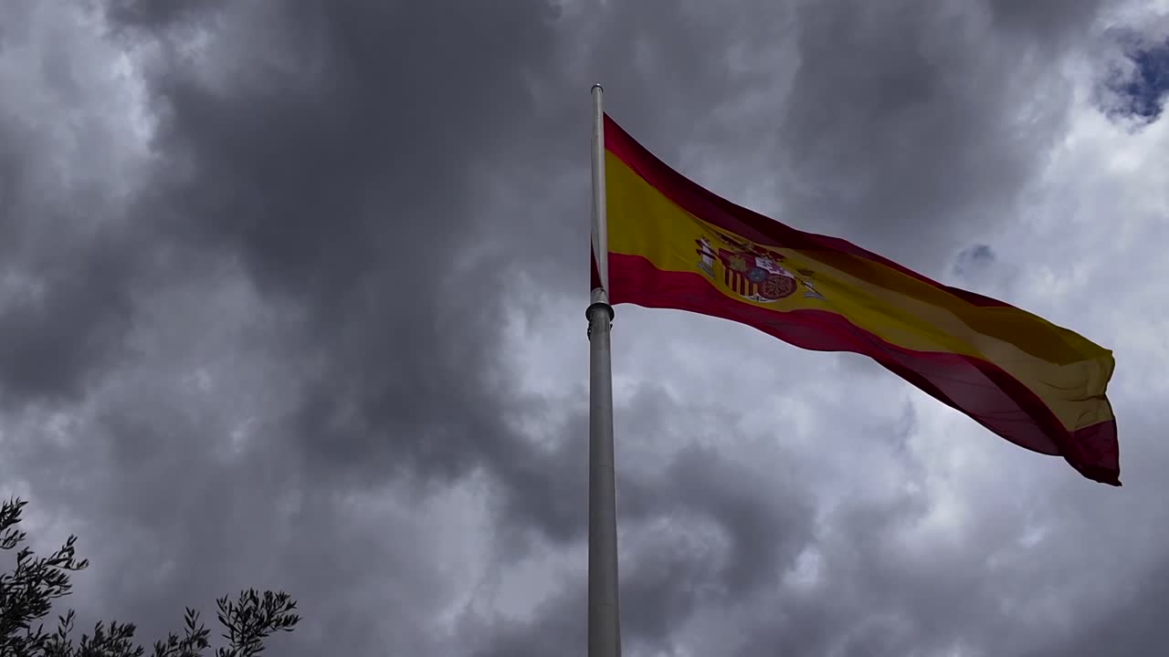 극적인 폭풍우 하늘 아래에서 흔들리는 거대한 스페인 국기 의 낮은 각도 시각