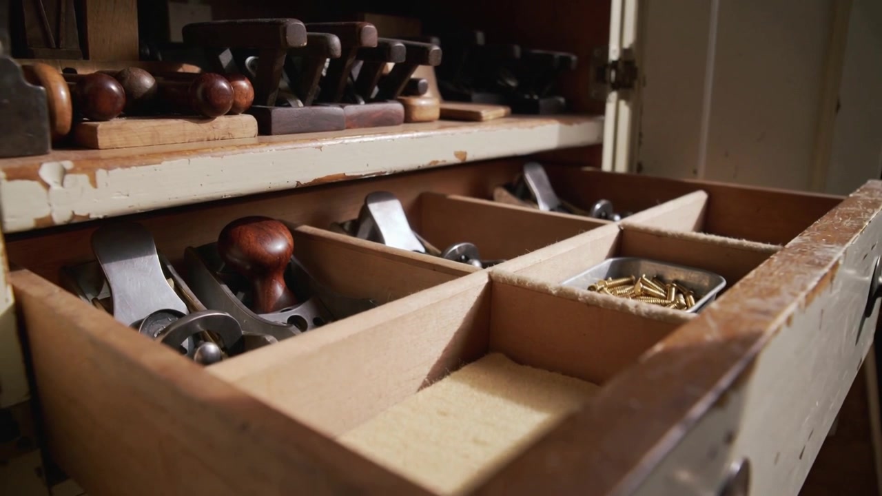 Ripresa con tracking della telecamera che mostra un cassetto scorrevole in legno, l'usura e la disposizione di pialle e viti in ottone in un'officina.