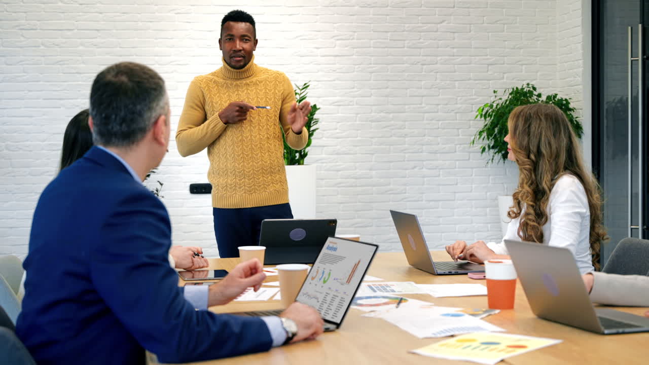 Chef d’équipe noir lors d’une réunion d’affaires dans un bureau, discutant des affaires de l’entreprise avec d’autres employés, documents et gadgets sur la table