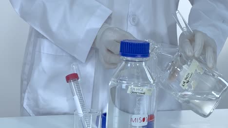 a scientist in a lab coat mixes clear liquids using labeled glassware and a pipette.
