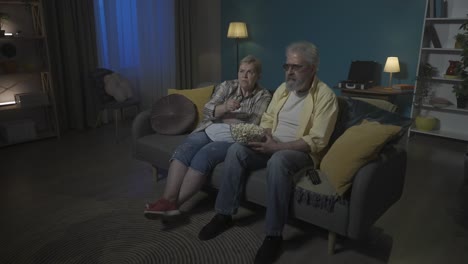 elderly couple watching tv and eating popcorn
