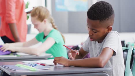 diverse female teacher and schoolchildren at desks in school classroom
