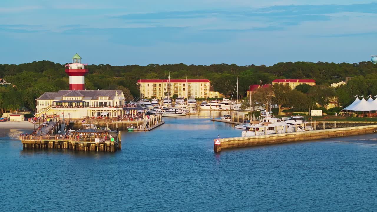 Aerial tracking establishing of harbor pier, bright rooftops, ocean glimmer and docked boats visible, Harbour Town Pier South Carolina USA