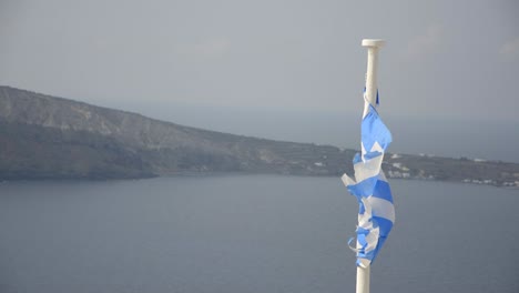 a slightly tattered greek flag blowing in the breeze in oia, on the island of santorini, greece