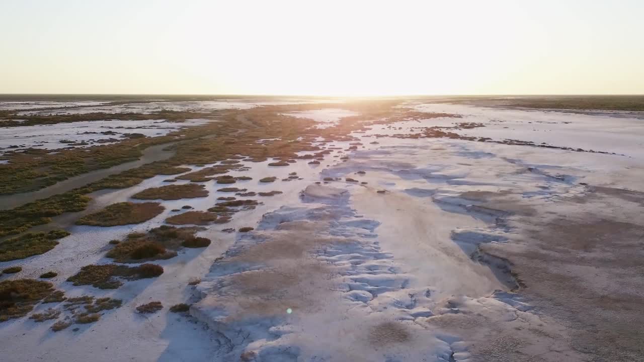 vista aérea en movimiento de un campo de sal, con poca vegetación y un cielo al atardecer
