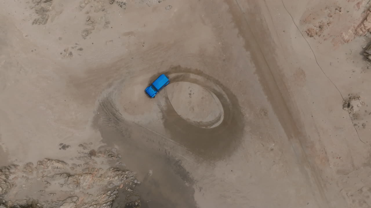 A blue car drifting on a sandy coastal road in oman, aerial view