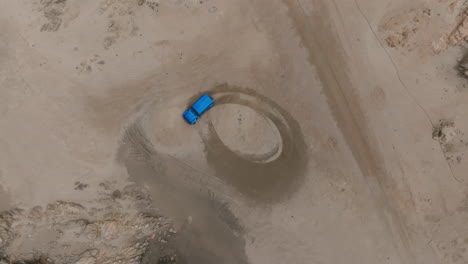 a blue car drifting on a sandy coastal road in oman, aerial view