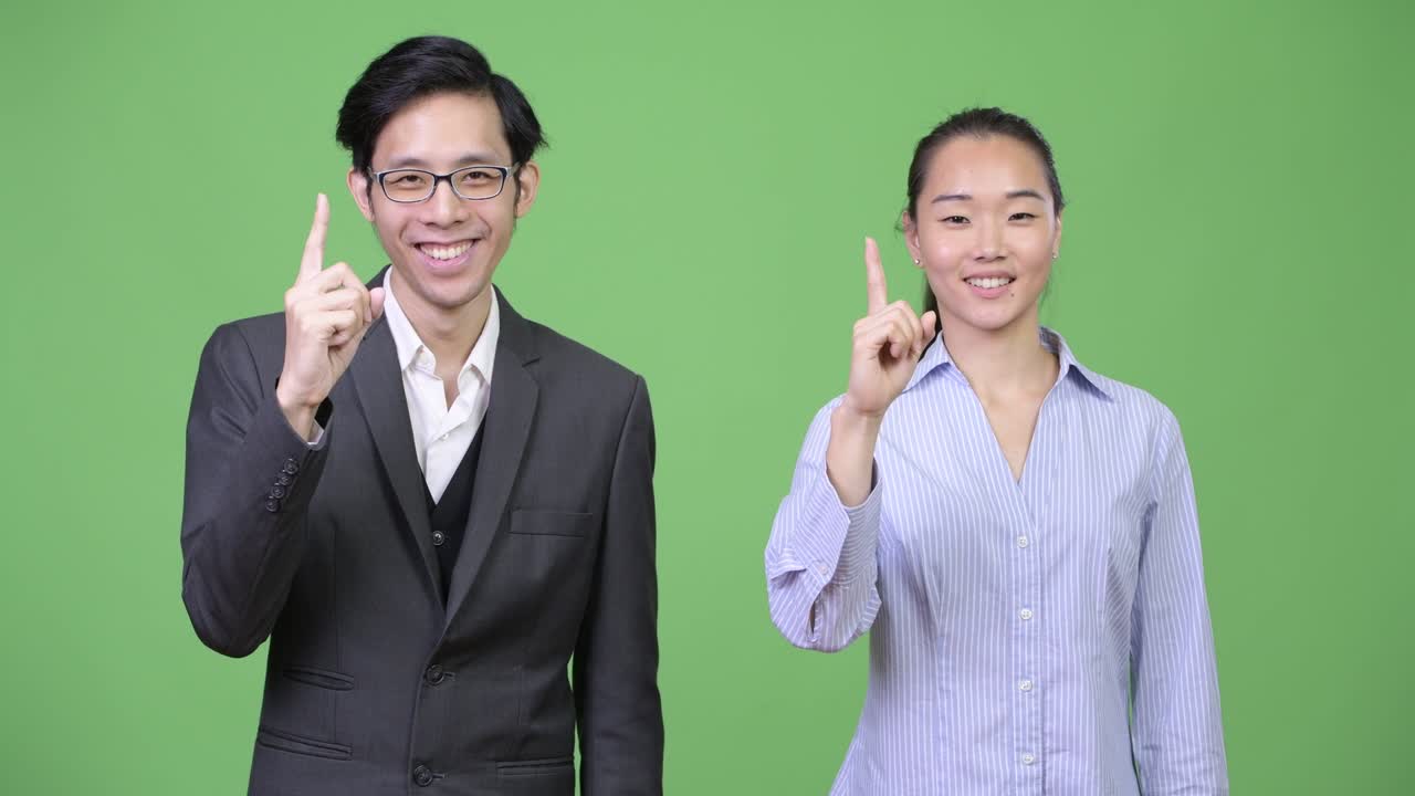 Young Asian business couple pointing up together