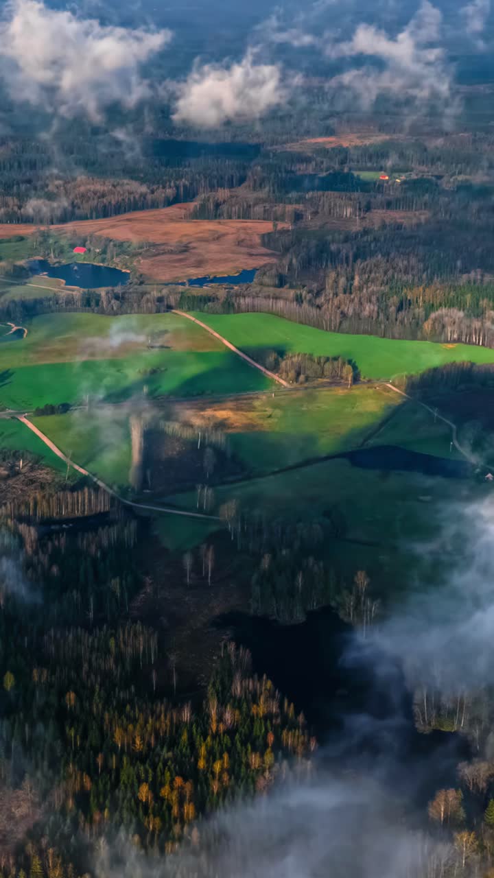 Morning fog drifts across green pastures and forested lowlands in drone hyperlapse