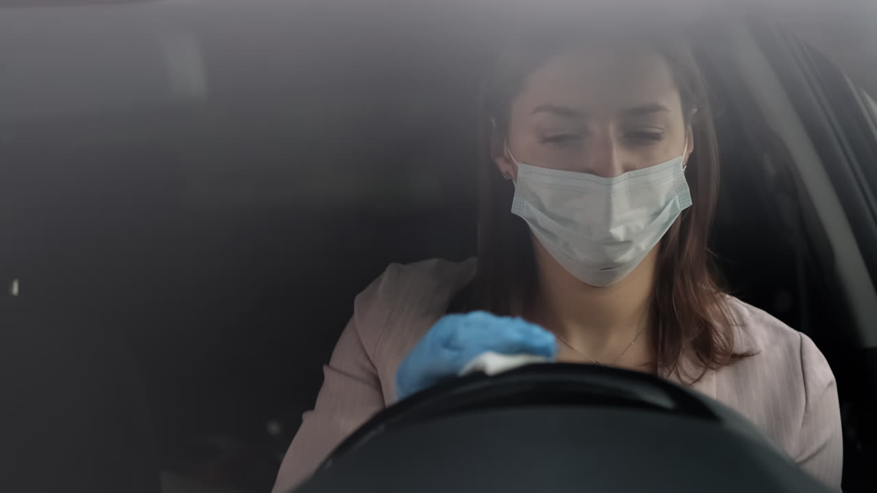 mujer limpiando el volante del coche usando máscara y guantes