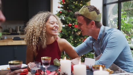 Couple-Sitting-Around-Dining-Table-At-Home-For-Christmas-Dinner-With-Friends-Talking-And-Whispering