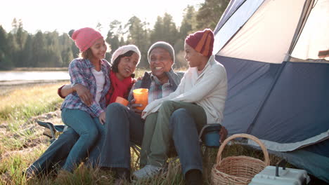 Grandparents-and-grandchildren-relaxing-outside-tent-by-lake