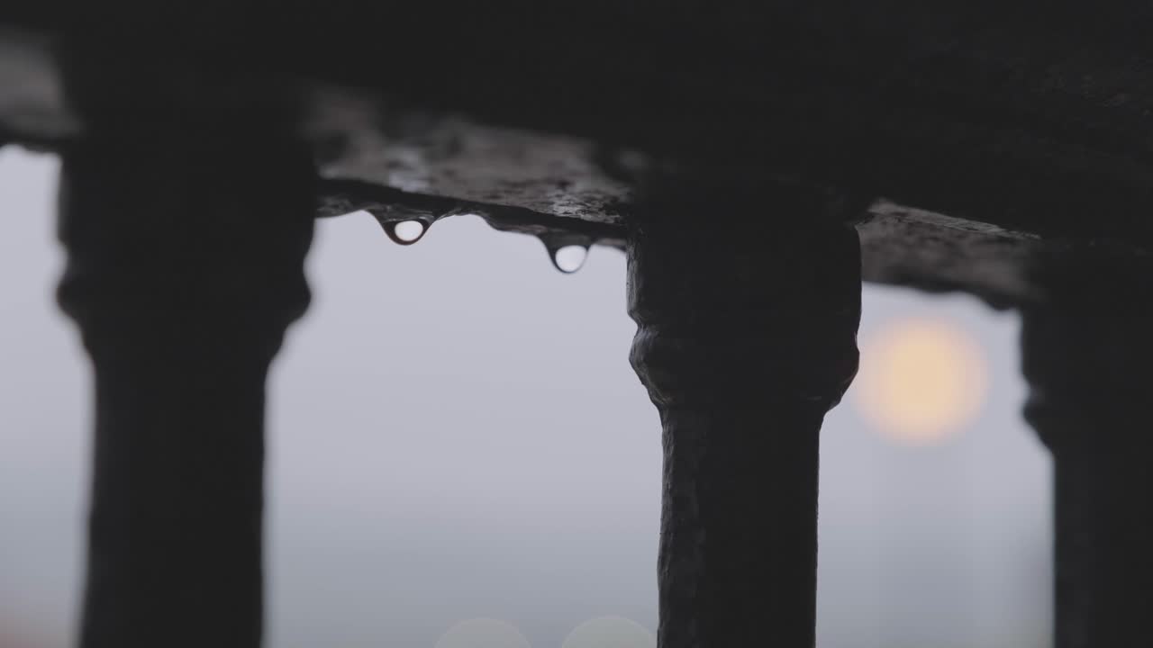 Raindrops on iron railing with blurred street lamp glowing in the background on an overcast day in Hondarribia, Spain