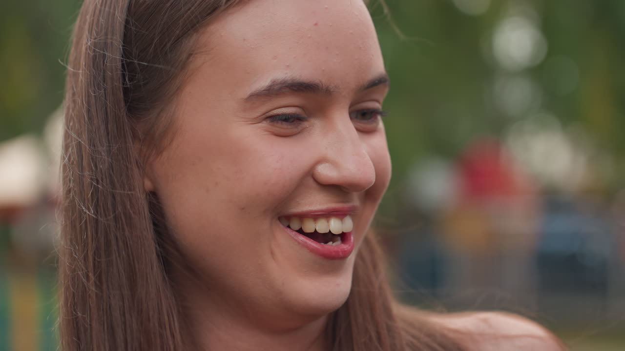 Adolescente branco sorrindo em festival, namorado por perto, conversa íntima e risadas compartilhadas criam uma atmosfera divertida, brinquedos coloridos e cerca de madeira ao fundo, expressões espontâneas mostram uma conexão crescente