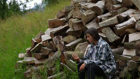 teenager sitting in a forest with a pile of wood, reading a book