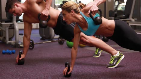 Two-fit-people-lifting-kettle-bells-together-in-plank-position