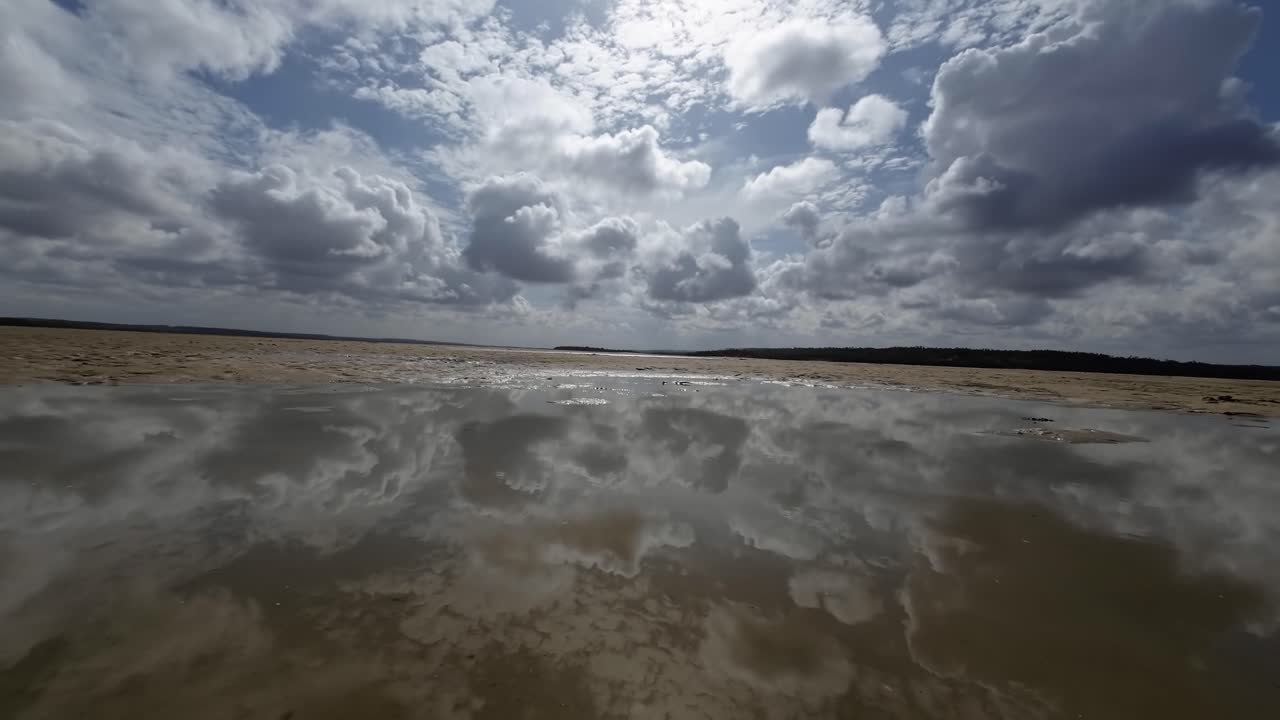 Dolly in landscape worms eye view shot of a tropical wet sand bar during low tide in the Guara&iacute;ras Lagoon of Tibau do Sul, Brazil in Rio Grande do Norte during a sunny summer cloudy day near Pipa