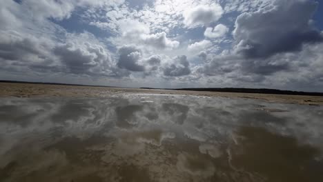 dolly in landscape worms eye view shot of a tropical wet sand bar during low tide in the guaraíras lagoon of tibau do sul, brazil in rio grande do norte during a sunny summer cloudy day near pipa