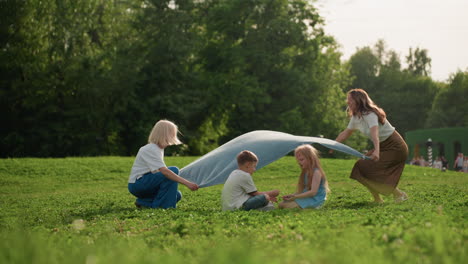 summer children seated on grass while mother spreads picnic blanket under sunny sky, face painted girl and boy sharing playful moment, green park background, warm light and gentle breeze