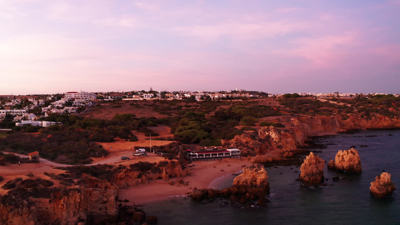 Ripresa aerea di un paesaggio rosso al tramonto che mostra l'acqua dell'oceano, la spiaggia e un resort alberghiero in cima alla collina