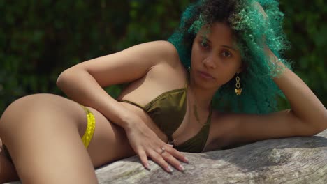 a young girl with a light complexion, wearing a bikini, reclines on a fallen tree log at the beach