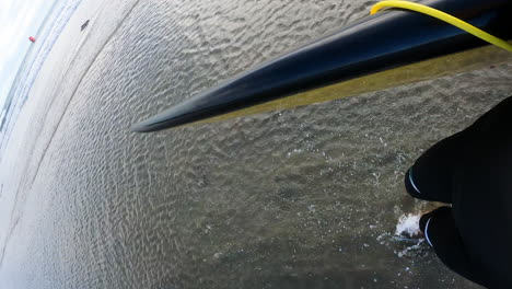 person walking along sandy beach carrying surfboard pov