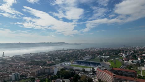 Antena-Diurna-De-Una-Zona-Residencial-De-Viviendas-Urbanas-Con-Instalaciones-De-Estadio-De-Fútbol,-Superficie-De-Agua-Del-Océano-Visible-En-La-Distancia,-Ubicación-Portugal