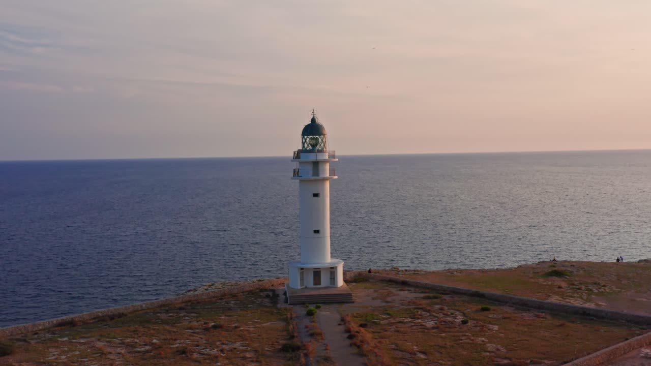 un faro increíble se alza al lado de un acantilado durante la majestuosa puesta de sol reflejándose en las aguas azules del océano, antena de drones
