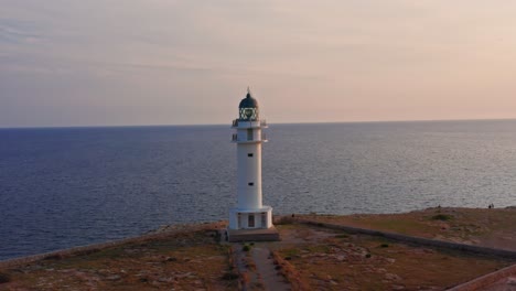 un faro increíble se alza al lado de un acantilado durante la majestuosa puesta de sol reflejándose en las aguas azules del océano, antena de drones