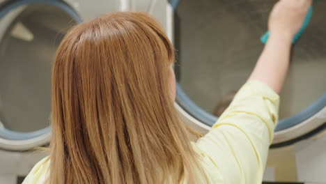 close up of business woman in yellow shirt cleaning washing machine door with soapy towel, focusing on surface wiping action with professional care inside laundry facility