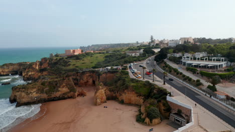 Amazing-aerial-drone-view-of-Portuguese-coastline,-drone-flying-sideway-above-road-in-Lagos-reveal-tourist-attraction-beaches,-Algarve,-day