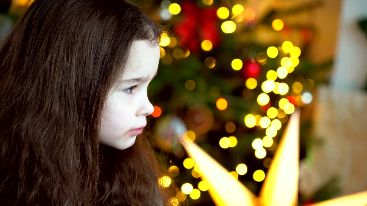 크리스마스 트리 근처에 앉아있는 행복한 어린 소녀의 초상화 새해 전날 꾸며진 방에서 새해와 휴일과 어린이 개념과 함께 축제 휴일 축제를 즐기고 있습니다.