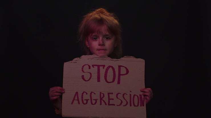 Bambina senzatetto povera e impaurita con il viso sporco, che mostra uno striscione con il messaggio 'Stop all'Aggressione'.