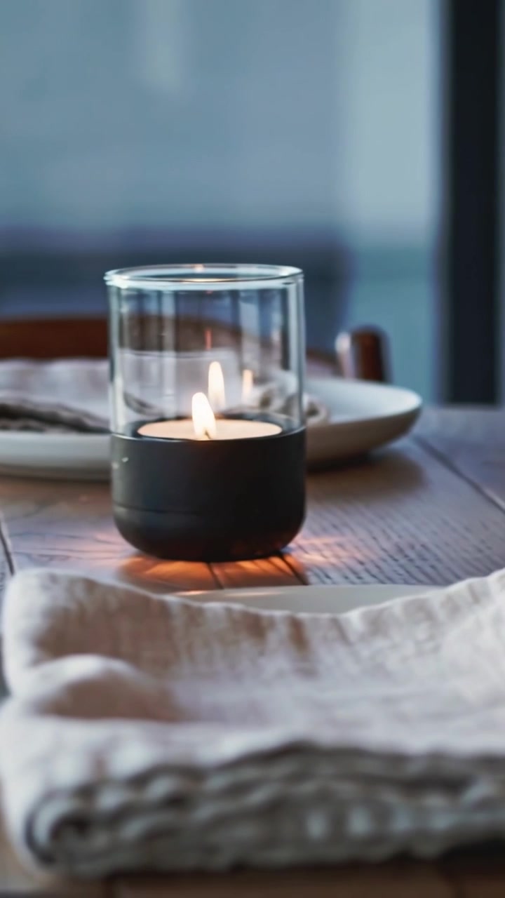 Vertical video: Panning camera revealing wood table at window, showing plates, napkins, lit candle